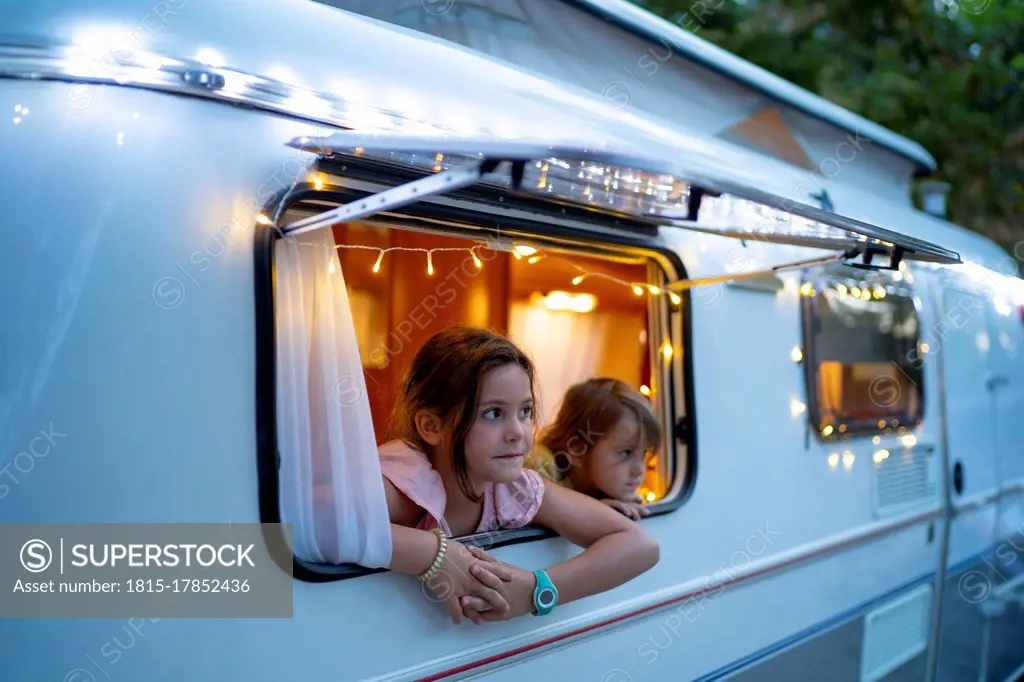 Cute sisters looking through window of illuminated motor home at dusk