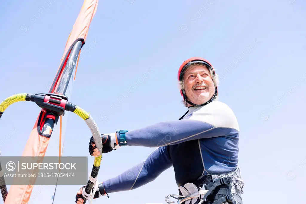 Cheerful senior man windsurfing against clear sky during sunny day
