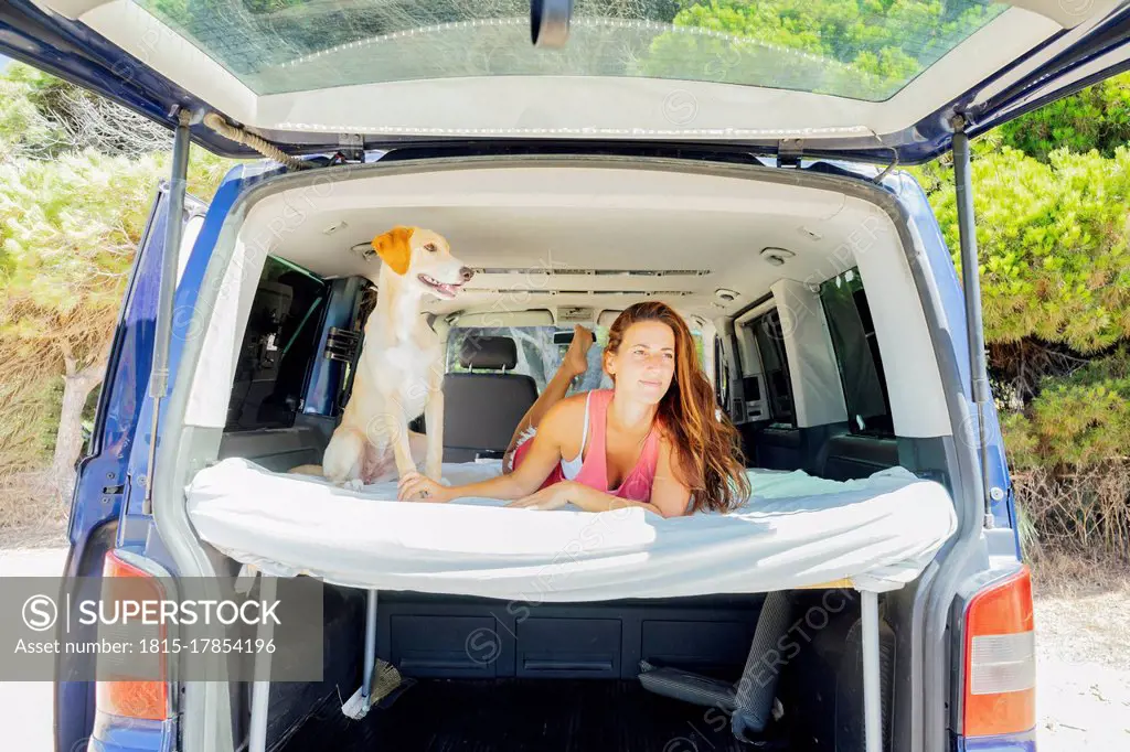 Woman with dog lying on bed in motor home at beach