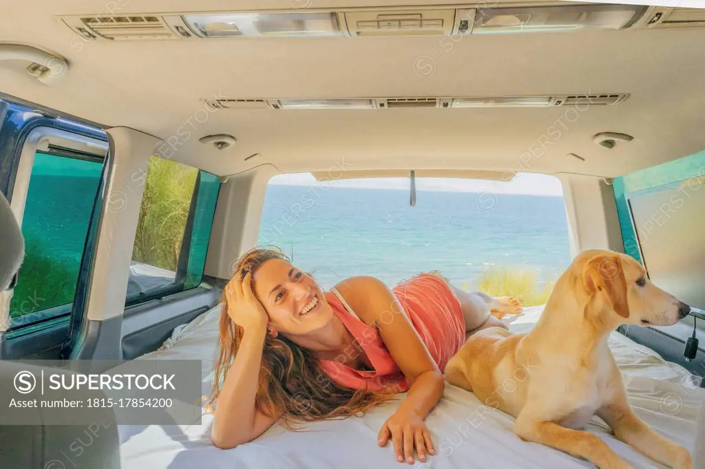 Smiling mid adult woman with dog relaxing on bed in motor home against sea