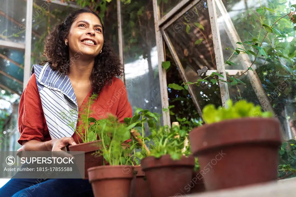 Mature woman smiling while looking away holding plant sitting in garden shed