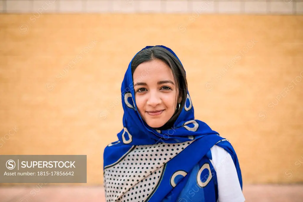 Young woman wearing scarf standing against wall