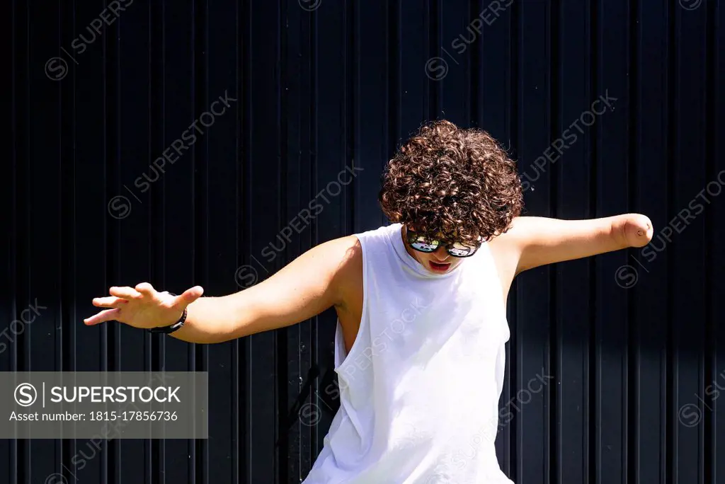Amputee teenage boy dancing against shutter on sunny day