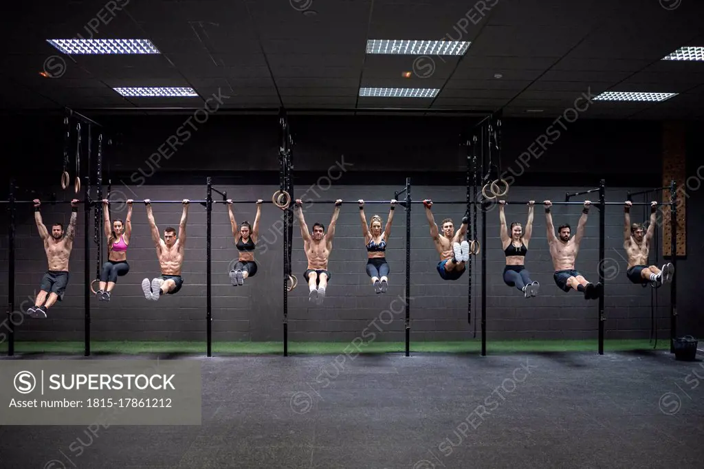 Male and female athletes hanging on rod at gym