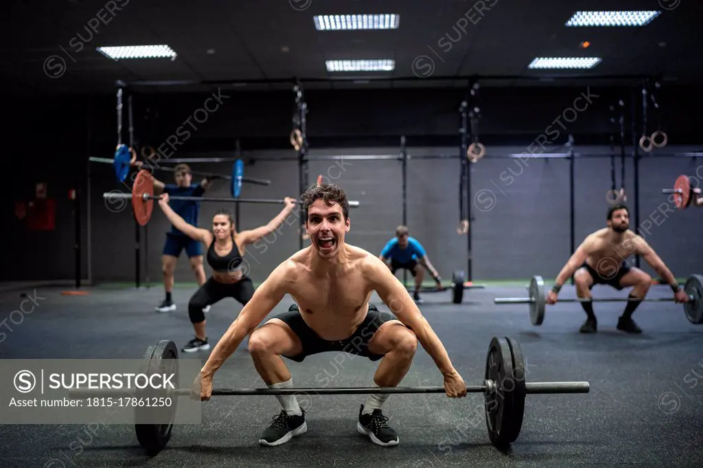 Athletes picking barbell while exercising at gym