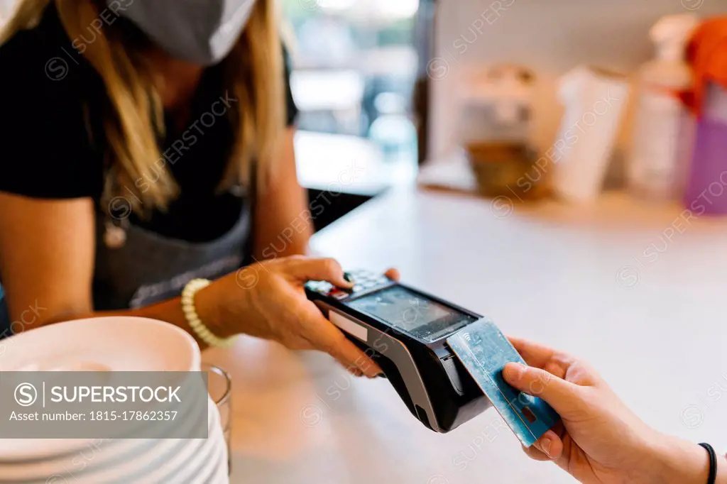 Female cashier receiving payment through credit card from customer in cafe during COVID-19