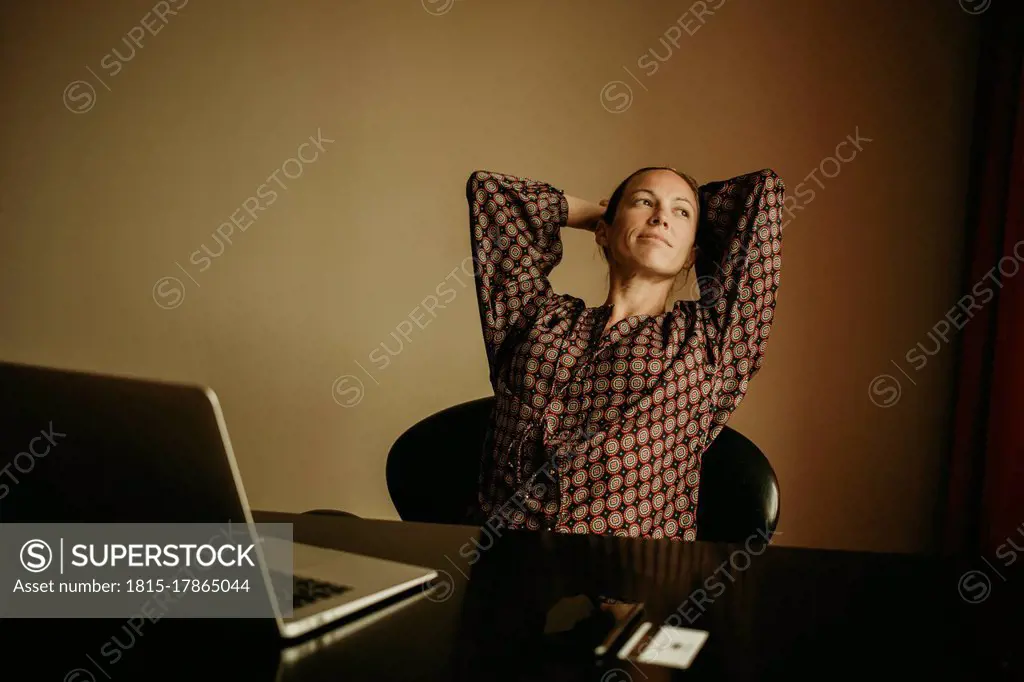 Businesswoman with hands behind head looking away while sitting in office