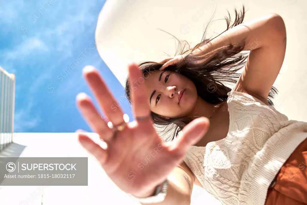 Young woman with hand in hair doing stop gesture on sunny day