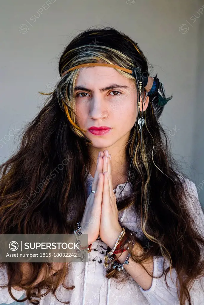 Close-up of hippie woman standing in prayer pose against wall