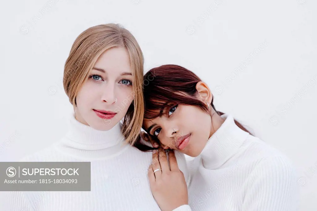 Young woman leaning on girlfriend's shoulder against white background