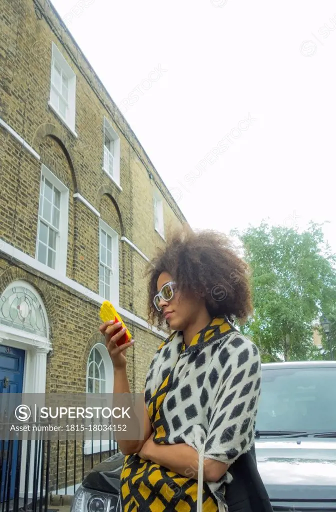Woman using mobile phone while standing by car