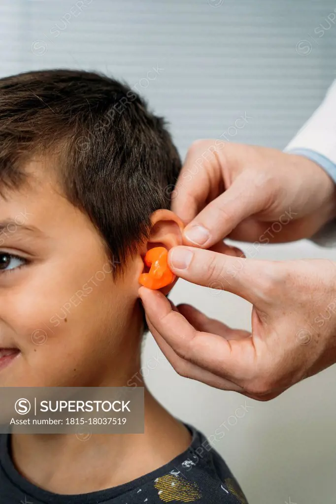 Male audiologist putting hearing air in child's ear at clinic