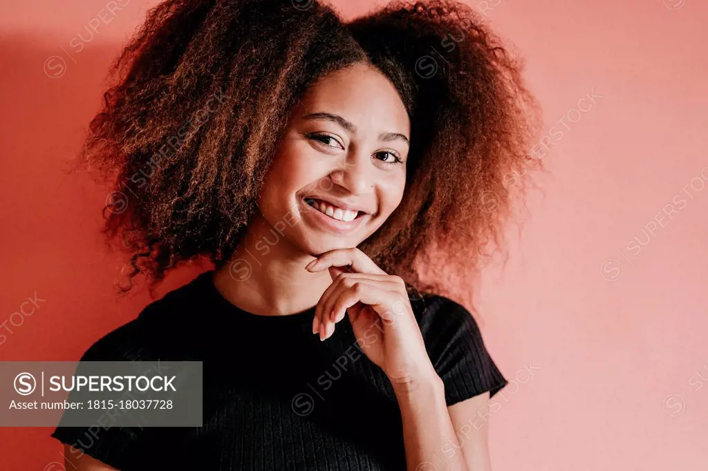 Happy Afro woman with hand on chin against peach background