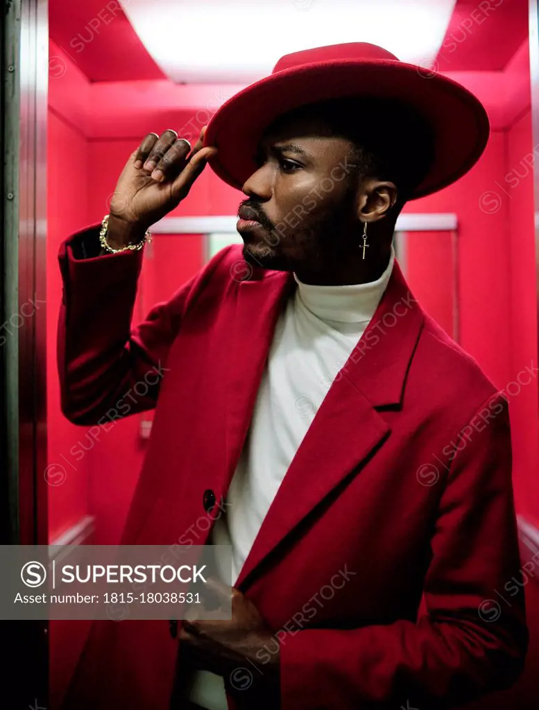 African fashionable man holding hat while peeking outside elevator