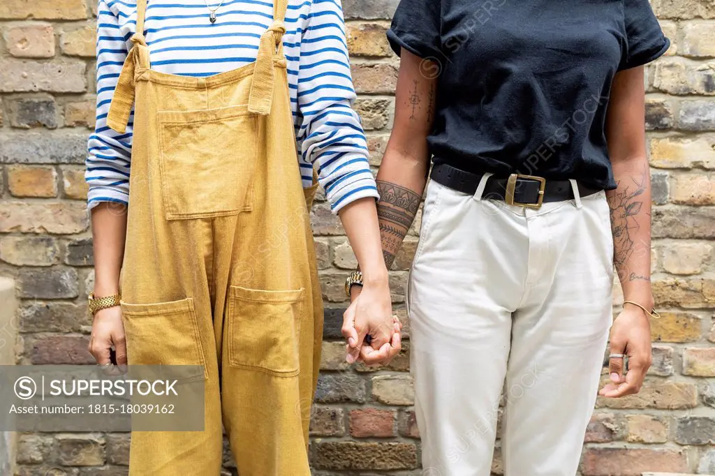Young lesbian couple holding hands while standing against brick wall