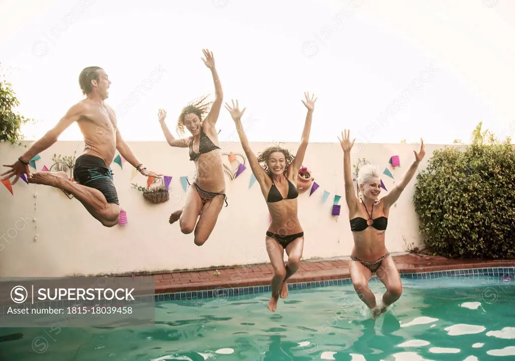 Carefree friends jumping together into swimming pool against sky during sunset