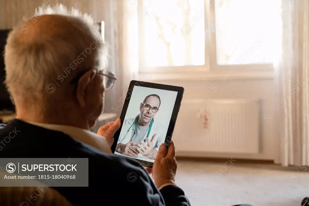 General practitioner consulting senior man online through digital tablet in living room