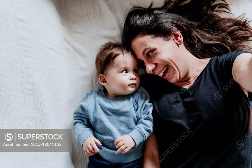 Smiling mother and son taking selfie while lying down on bed at home