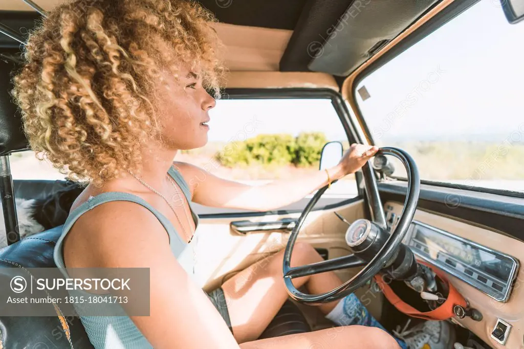 Young blond Afro woman sitting in old off-road vehicle