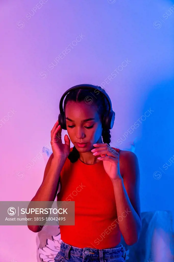 Thoughtful woman listening music through headphone sitting at home
