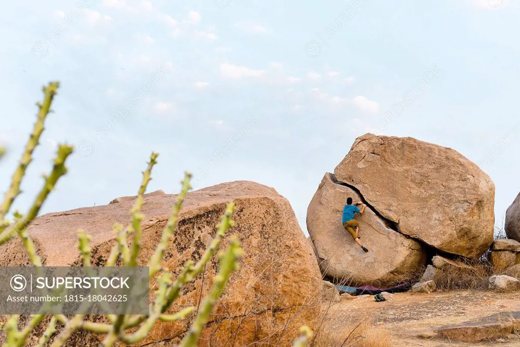 Determinant young man boulderer climbing rock, Karnataka, Hampi, India