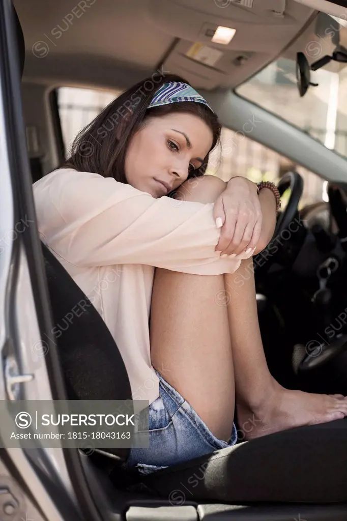 Sad woman hugging knees while sitting in car