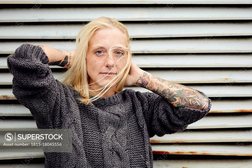 Tattooed woman with hand in hair standing in front of shutter