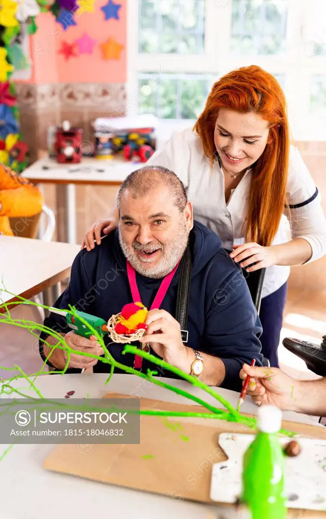 Smiling man doing craft with female nurse in nursing home