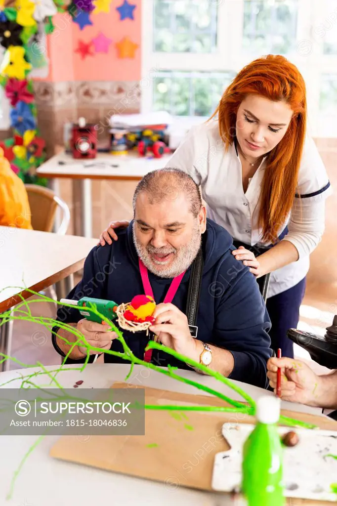 Disabled man doing craft with female caregiver in rehabilitation center