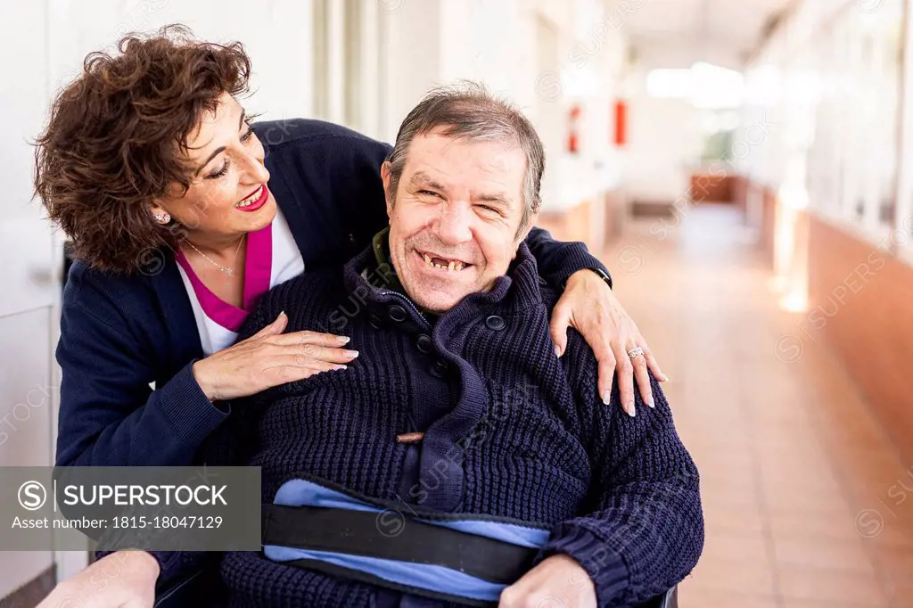 Happy nurse looking at disabled man in corridor of nursing home