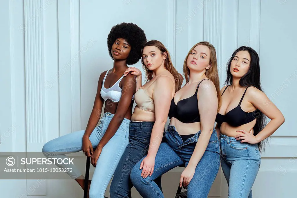 Multi-ethnic group of women wearing bras and jeans against wall - SuperStock