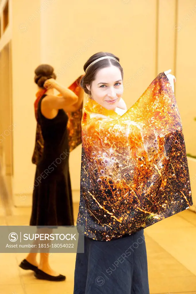 Smiling woman showing printed Chakra 3 on silk cloth while standing against mirror