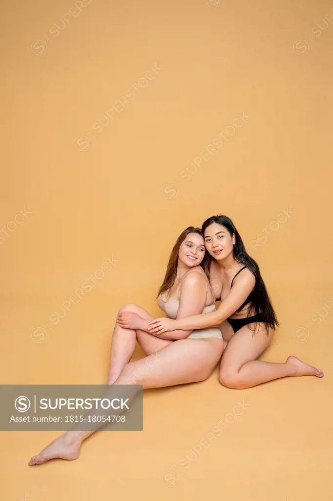 Smiling multi-ethnic female models in lingerie smiling posing against yellow background