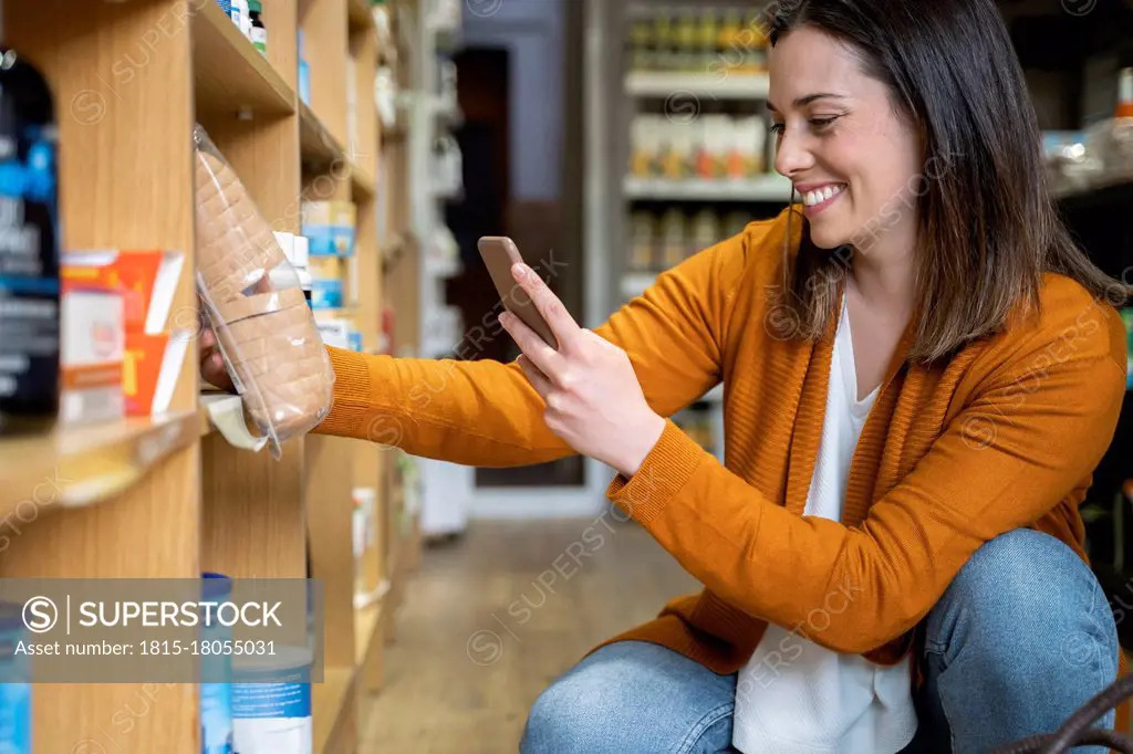 Happy young woman photographing package in grocery store