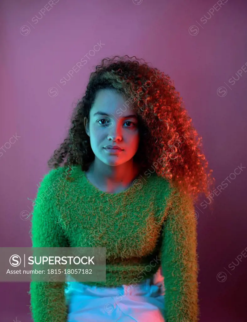 Red light on fashionable woman with curly hair sitting against pink background