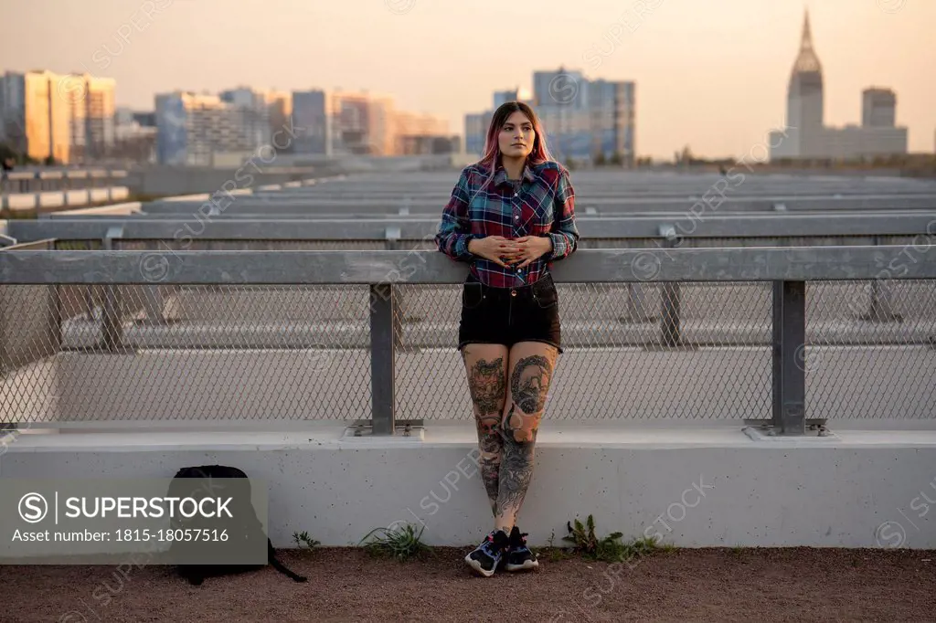 Fashionable woman day dreaming while leaning on railing at rooftop during sunset