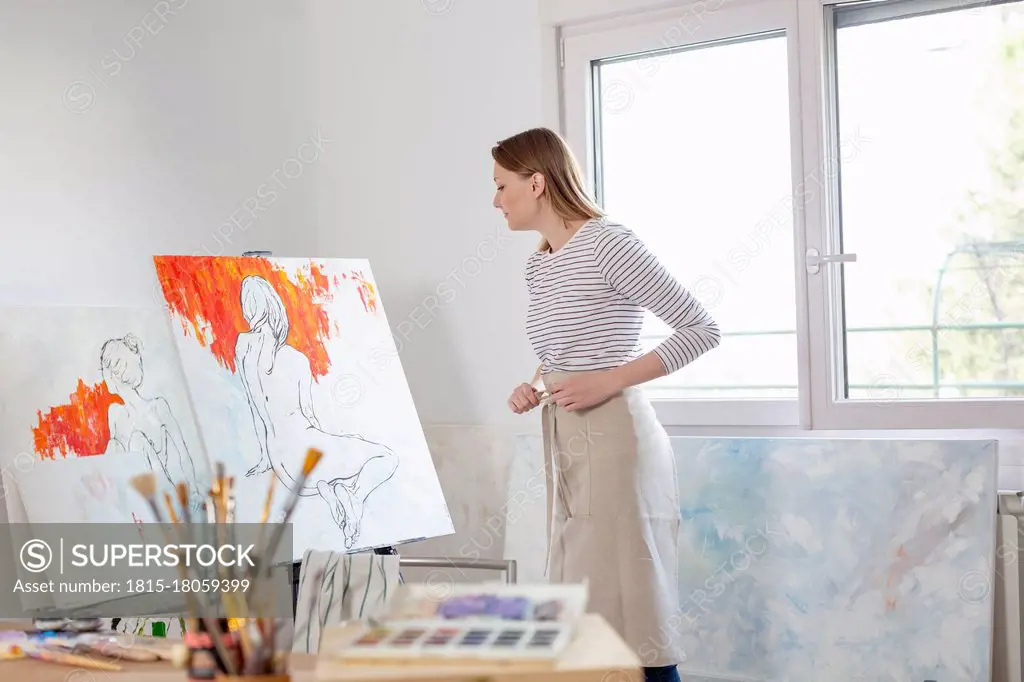 Female artist looking at canvas in home studio