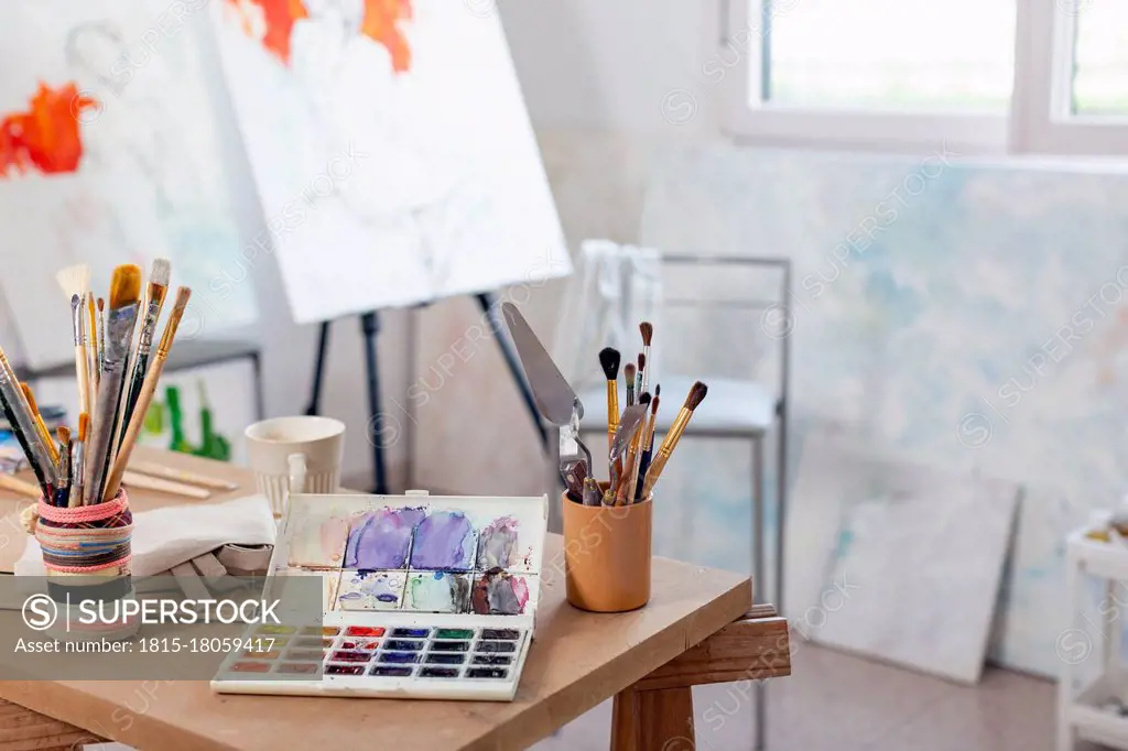 Artist's canvas and variety of paintbrush on table at home studio