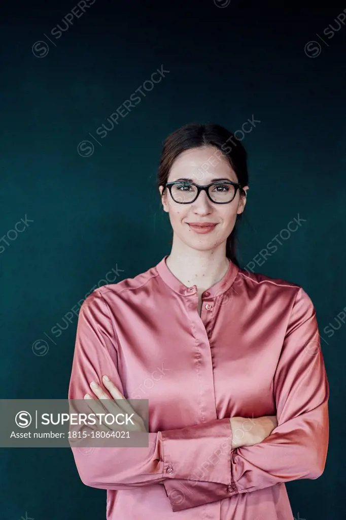 Smiling female entrepreneur with arms crossed against green background in studio