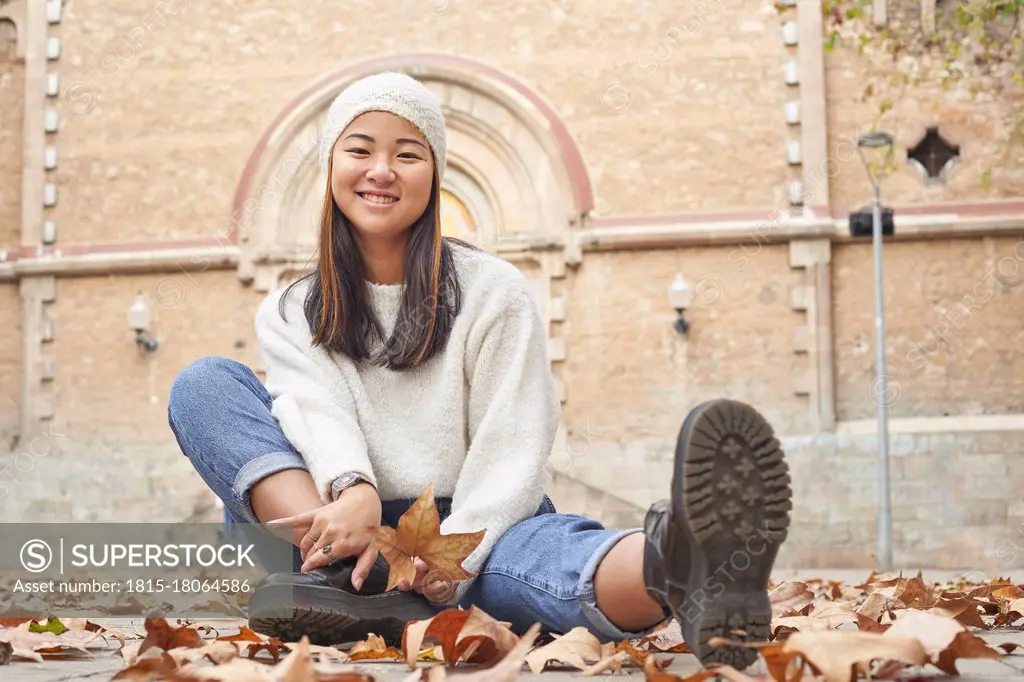 Smiling woman sitting by fallen dry leaf on footpath