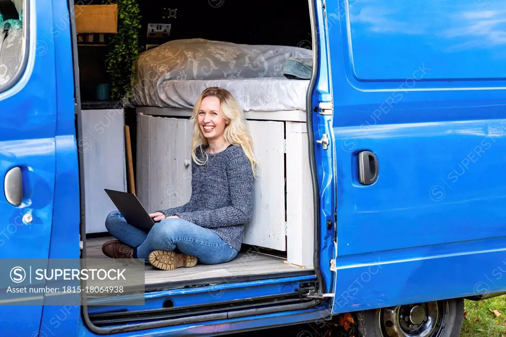 Happy woman with laptop sitting at door of camper van