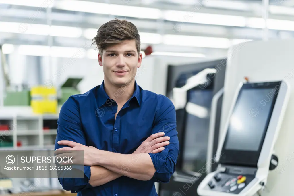 Handsome young male entrepreneur with arms crossed in industry