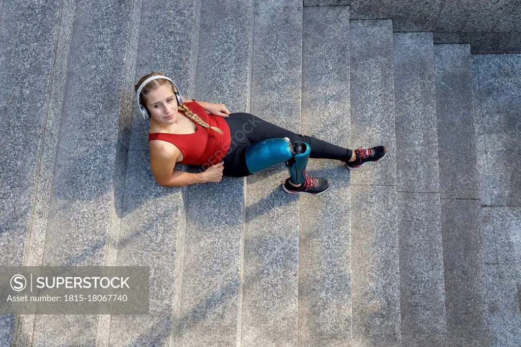 Young sportswoman with prosthetic leg relaxing while sitting on steps
