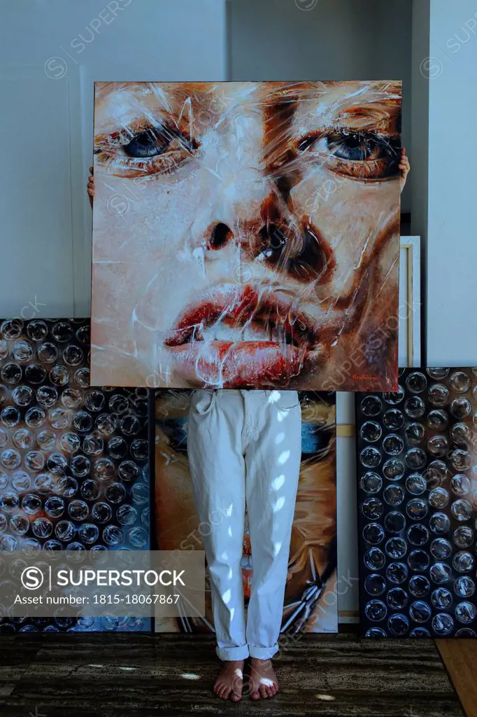Female artist standing behind painting against wall in art studio