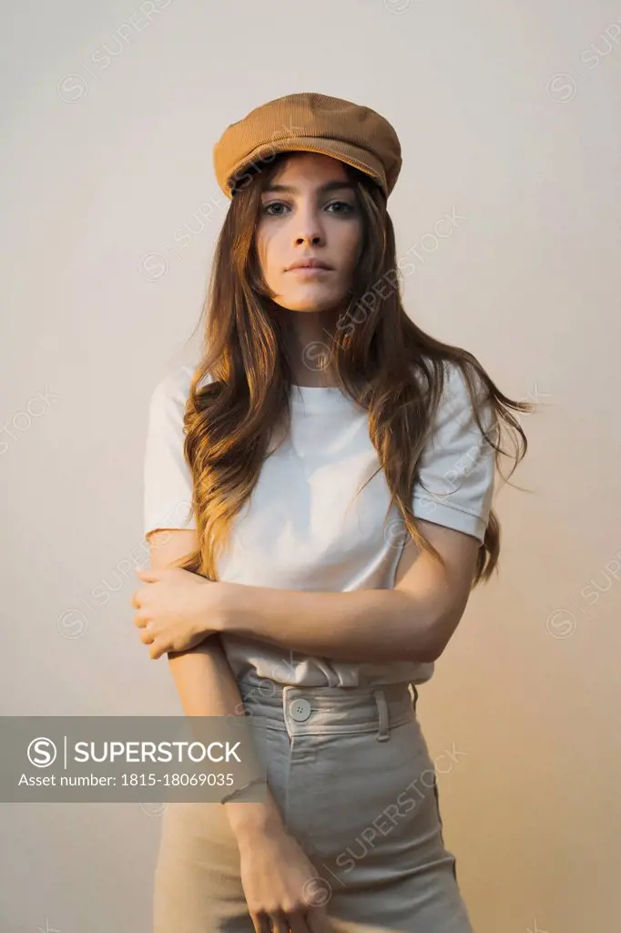 Woman wearing cap staring while standing against wall