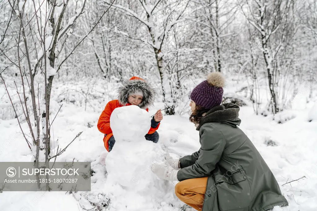 Girl with teenage sister making snowman in forest