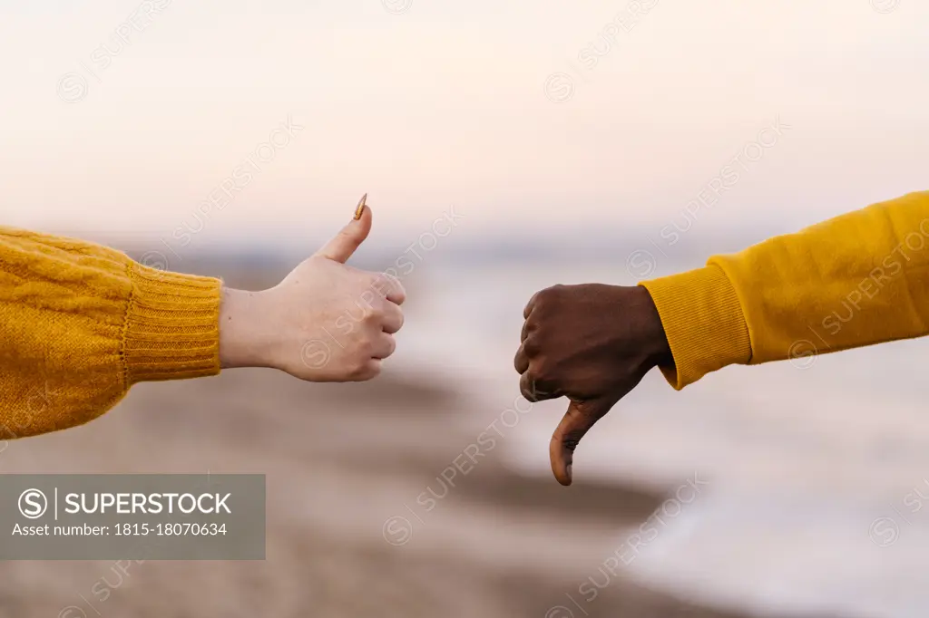 Woman and man showing thumps up and down gesture at beach