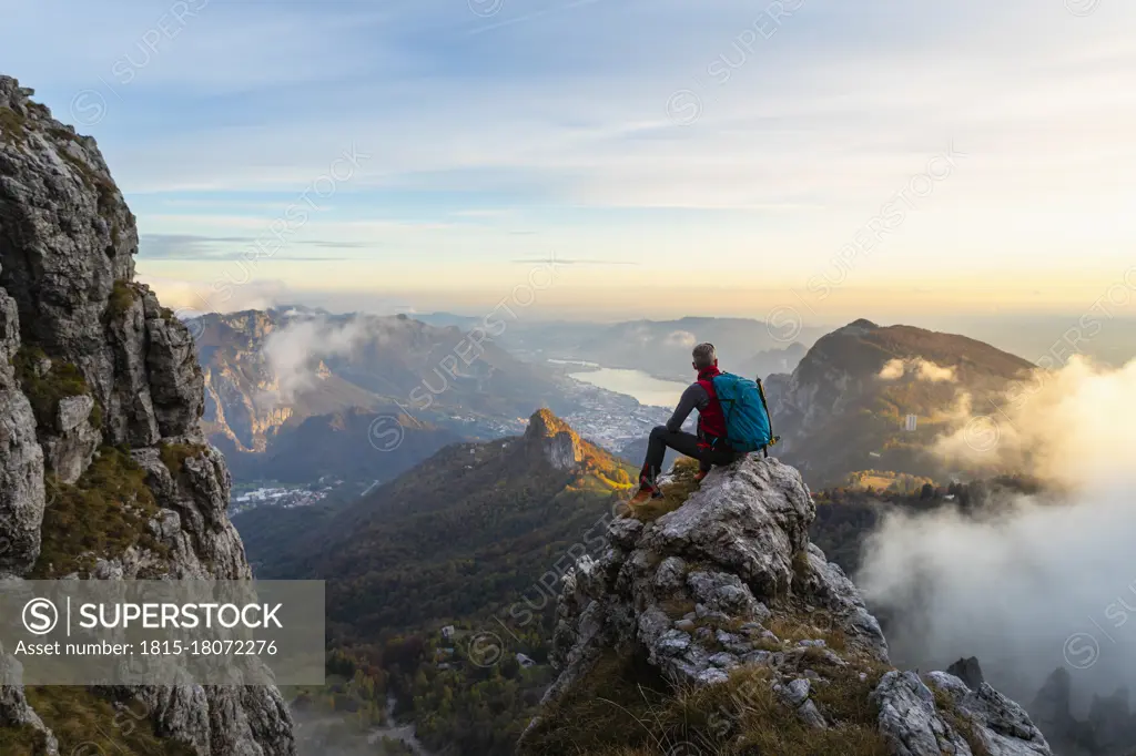 Pensive hiker looking at view while sitting on mountain peak during sunrise at Bergamasque Alps, Italy