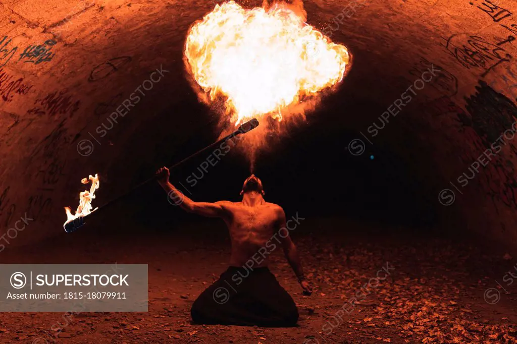 Male juggler performing with fire staff in dark tunnel
