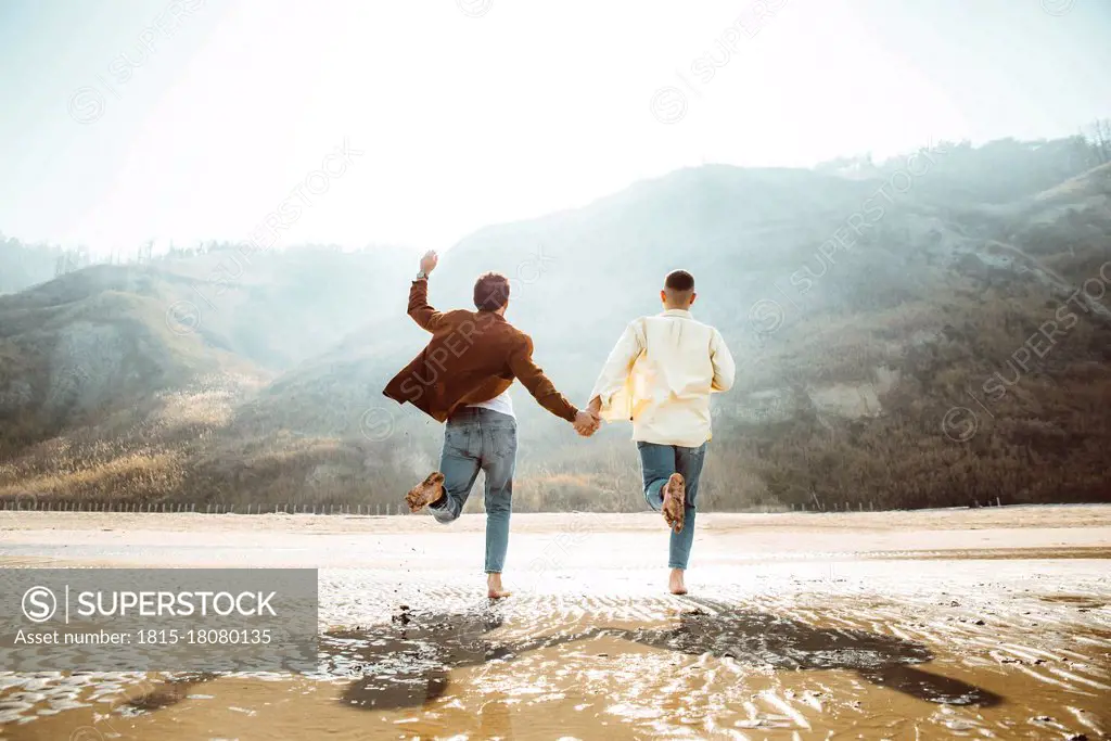 Homosexual couple holding hands and running at beach